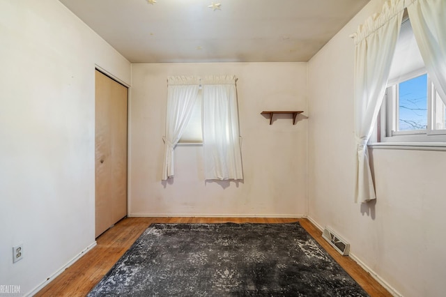 empty room with wood finished floors, visible vents, and baseboards