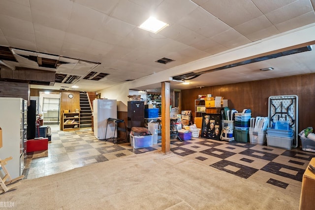 finished basement featuring tile patterned floors, wooden walls, stairway, and freestanding refrigerator