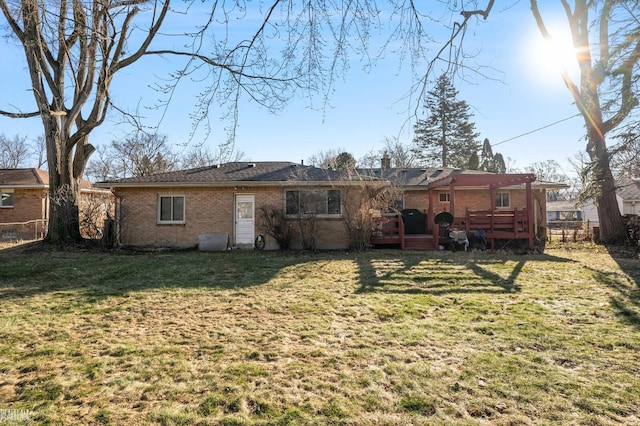 rear view of house with brick siding, a deck, a yard, and fence