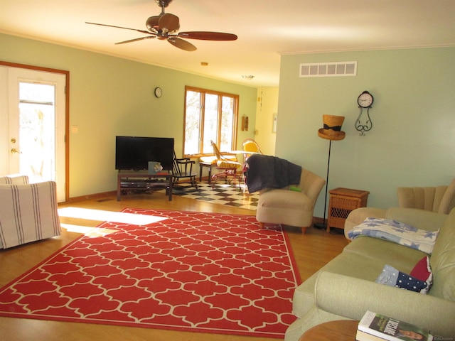 living area with ceiling fan, visible vents, wood finished floors, and ornamental molding