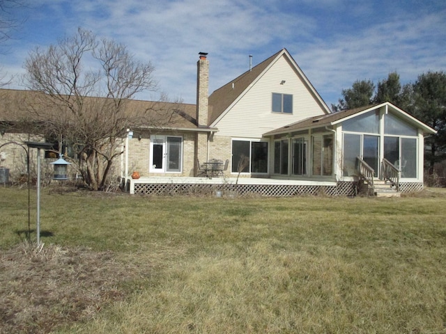 back of house featuring a sunroom, a chimney, entry steps, a lawn, and brick siding