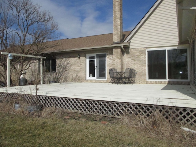 rear view of property with a deck, brick siding, and a chimney