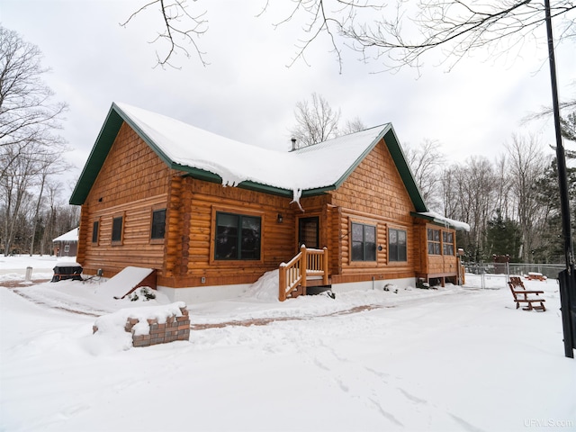 snow covered rear of property featuring log siding and fence