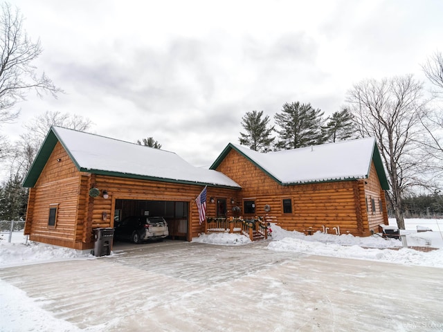 snow covered property featuring an attached garage, log exterior, and driveway