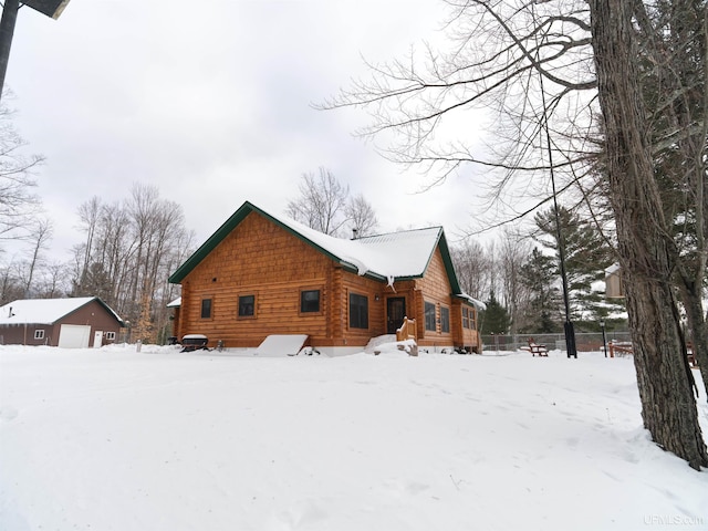 view of snowy exterior with a garage, an outbuilding, and fence