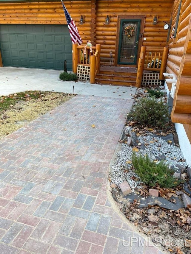 entrance to property featuring a garage, covered porch, log exterior, and driveway