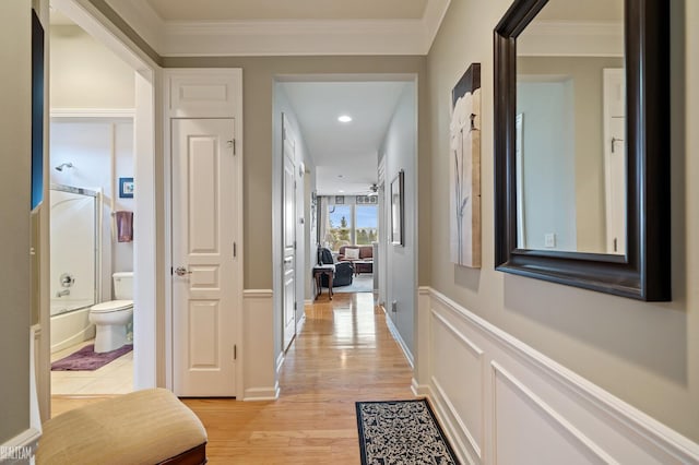 corridor with a wainscoted wall, a decorative wall, light wood-type flooring, and ornamental molding