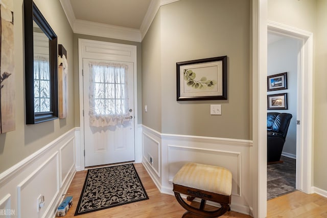 doorway to outside with light wood finished floors, a decorative wall, wainscoting, and crown molding