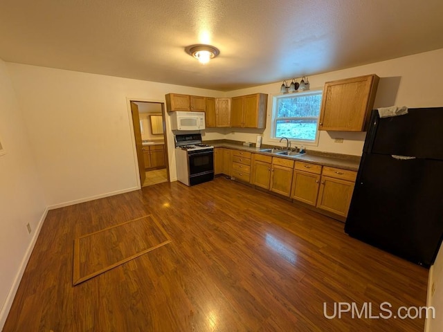 kitchen featuring dark wood-type flooring, a sink, gas range oven, freestanding refrigerator, and white microwave