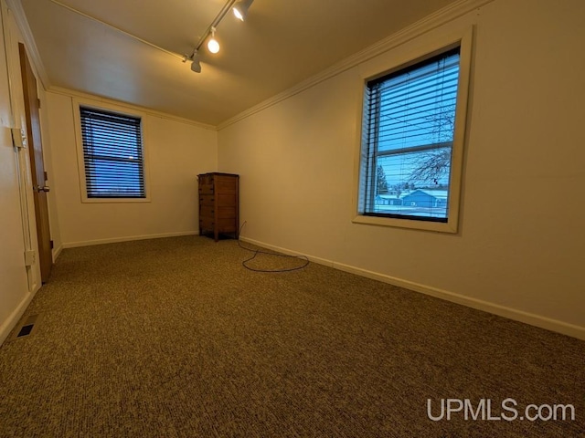 carpeted empty room with visible vents, rail lighting, crown molding, and baseboards