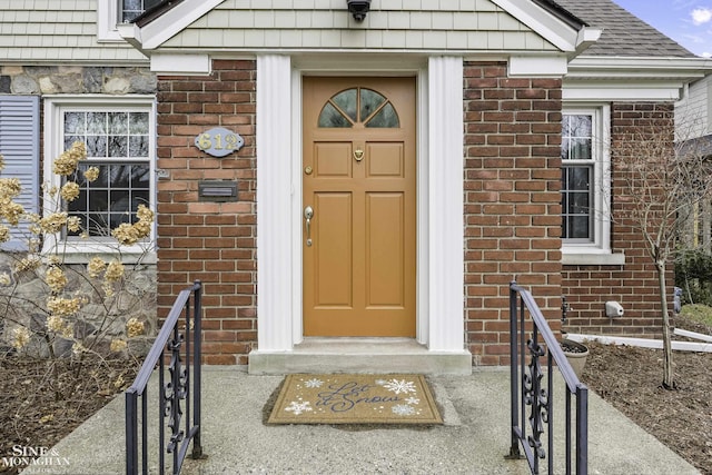 doorway to property featuring brick siding and a shingled roof