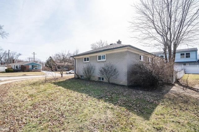 view of side of home featuring brick siding, a lawn, a chimney, and fence