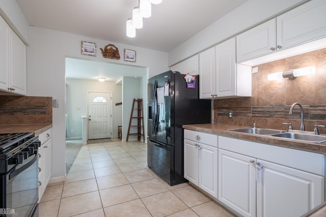 kitchen featuring light tile patterned floors, a sink, black appliances, white cabinetry, and backsplash