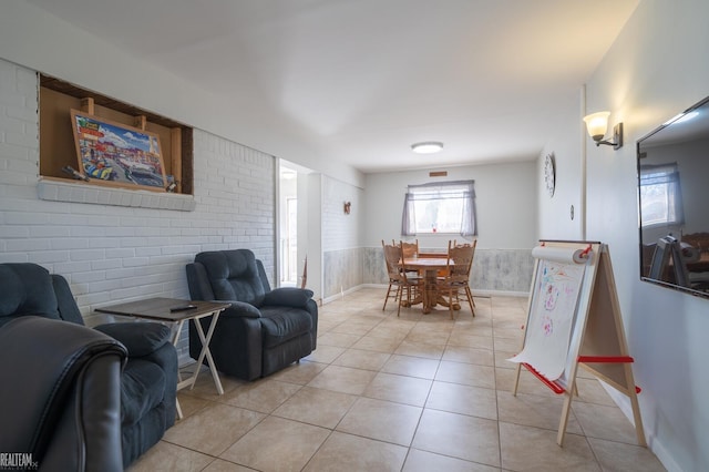 living area with light tile patterned flooring, a wainscoted wall, and brick wall