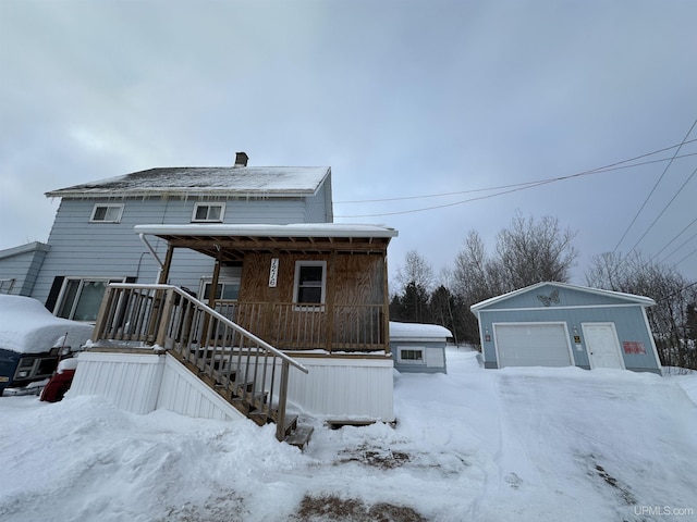 snow covered rear of property featuring a detached garage, a porch, and an outdoor structure