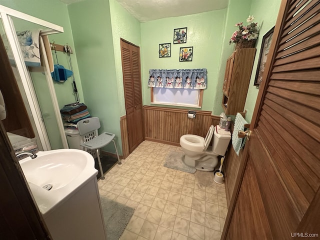 full bath with wooden walls, a wainscoted wall, toilet, a stall shower, and vanity