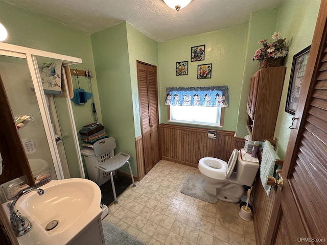 bathroom featuring toilet, a stall shower, a sink, a textured ceiling, and wood walls