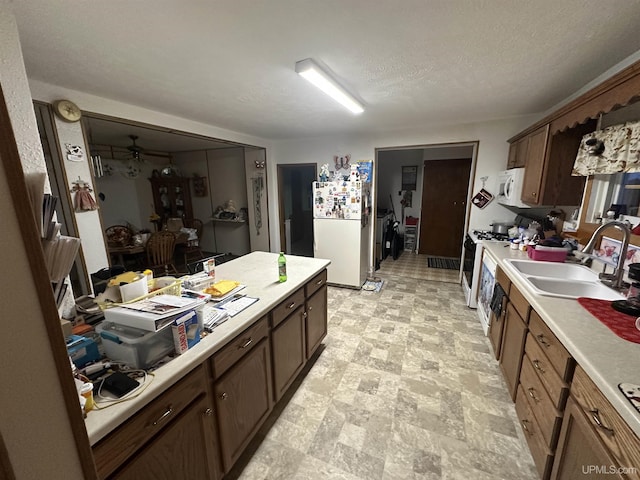 kitchen with a ceiling fan, a sink, a textured ceiling, white appliances, and light countertops