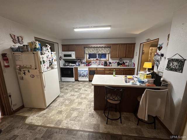 kitchen with a breakfast bar area, light countertops, brown cabinets, a peninsula, and white appliances