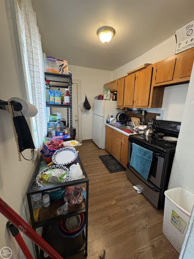 kitchen featuring stainless steel electric range oven, light countertops, freestanding refrigerator, brown cabinetry, and dark wood-style flooring