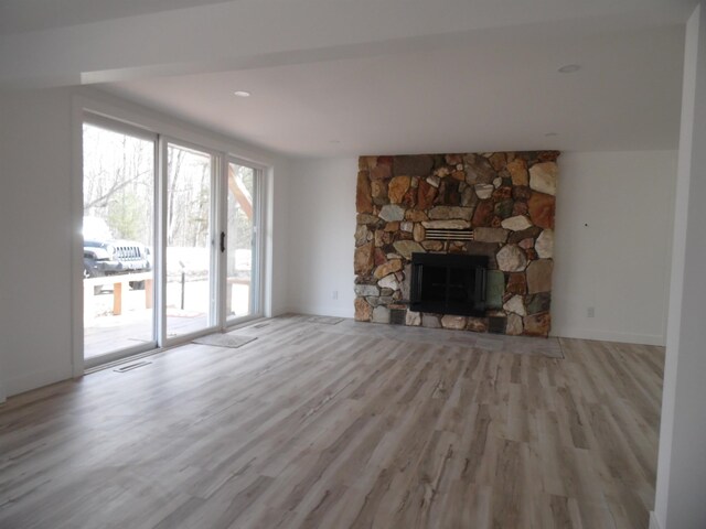 unfurnished living room with a stone fireplace, wood finished floors, visible vents, and baseboards