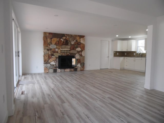 unfurnished living room featuring a stone fireplace, recessed lighting, light wood-type flooring, and a sink