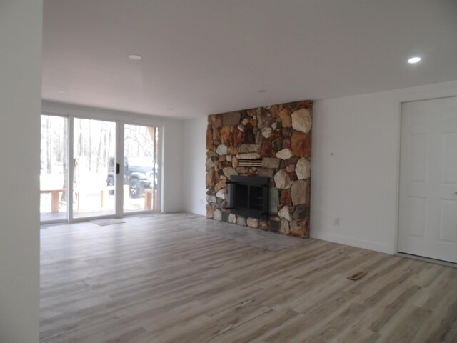 unfurnished living room featuring recessed lighting, a stone fireplace, and wood finished floors