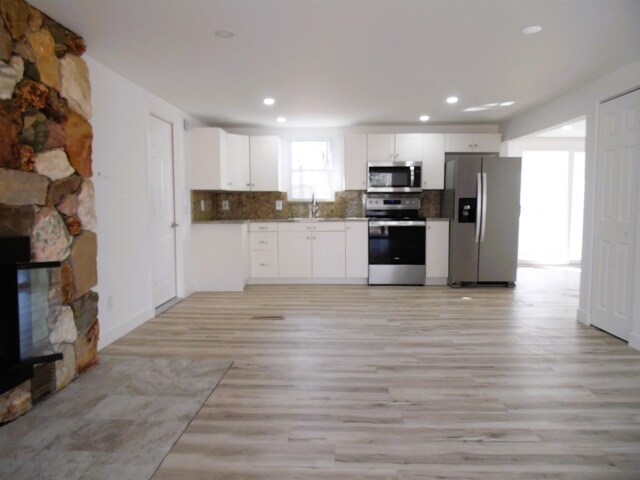 kitchen featuring tasteful backsplash, a stone fireplace, white cabinets, stainless steel appliances, and a sink