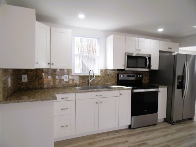 kitchen with white cabinets, stainless steel appliances, light wood-type flooring, and a sink