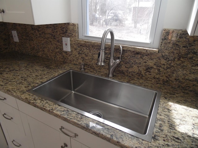 room details with decorative backsplash, white cabinets, light stone countertops, and a sink