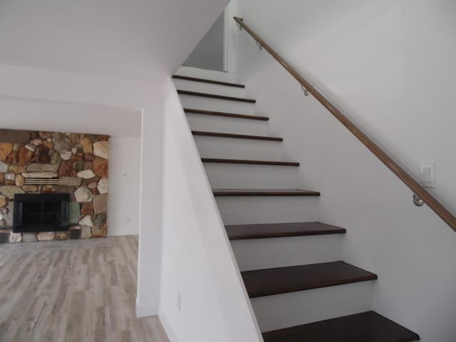 stairs with a stone fireplace and wood finished floors