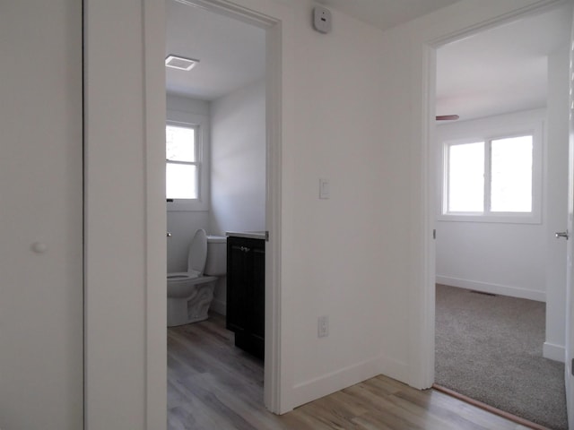 corridor featuring visible vents, baseboards, and light wood finished floors