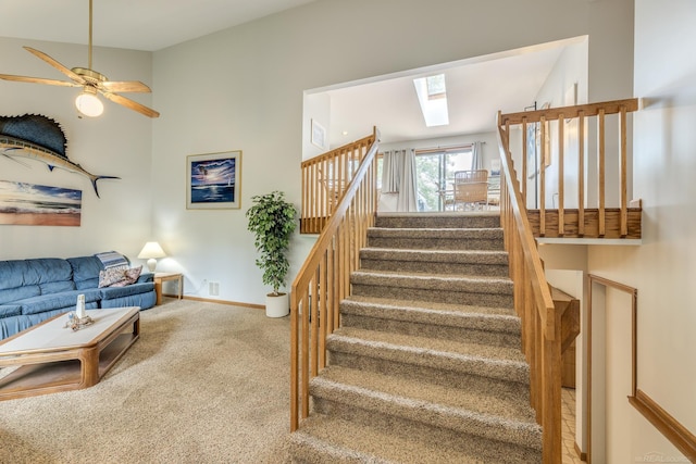 stairs featuring a ceiling fan, visible vents, baseboards, carpet floors, and a skylight