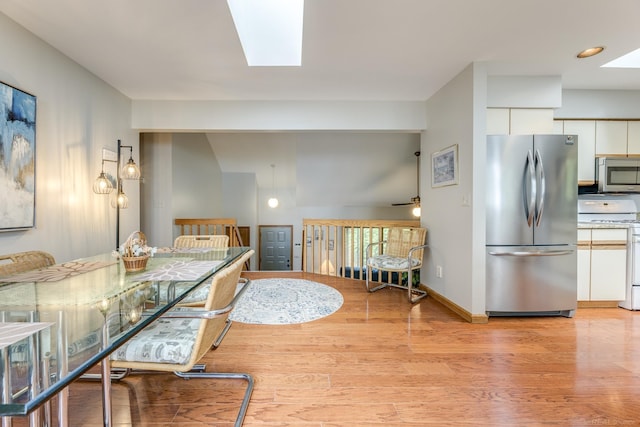 dining space featuring a skylight, light wood-style flooring, baseboards, and ceiling fan