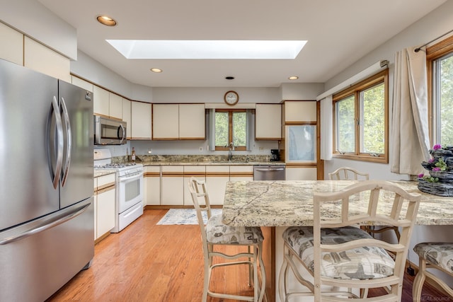 kitchen featuring light wood-type flooring, a sink, recessed lighting, stainless steel appliances, and a skylight