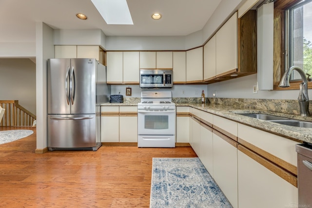 kitchen featuring light wood-style flooring, appliances with stainless steel finishes, a skylight, and a sink