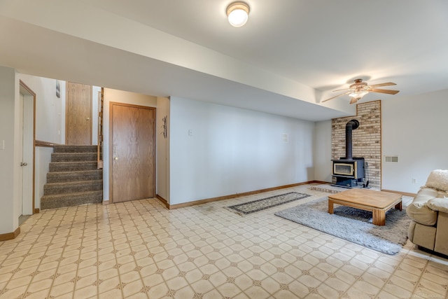 unfurnished living room featuring stairway, a wood stove, light floors, and baseboards