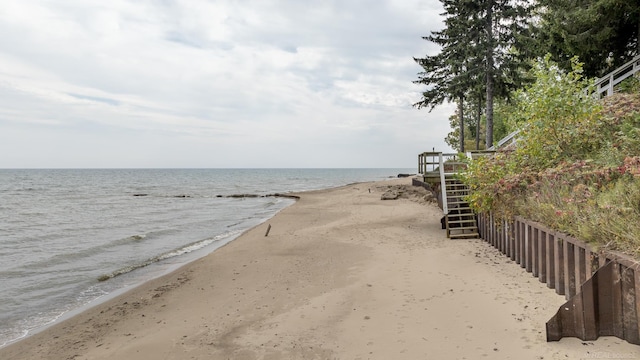 view of water feature featuring stairway, fence, and a beach view