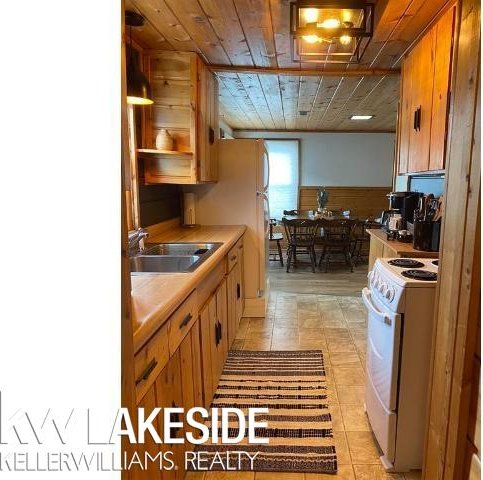 kitchen featuring brown cabinets, wood ceiling, white gas range oven, and a sink