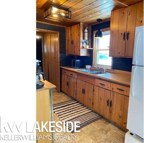 kitchen with wood ceiling, brown cabinets, freestanding refrigerator, and a sink