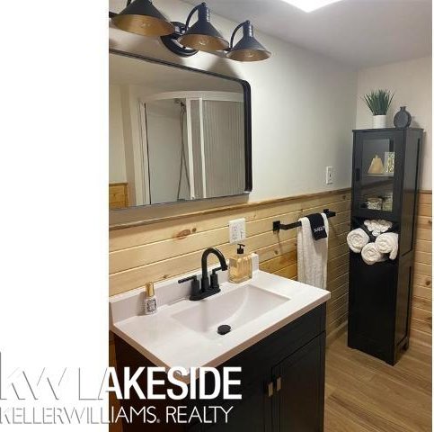 bathroom with a wainscoted wall, wood walls, vanity, and wood finished floors