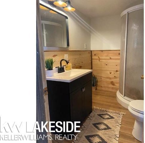 bathroom featuring vanity, wood finished floors, a shower stall, wainscoting, and toilet