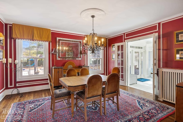 dining room with wood finished floors, a notable chandelier, ornamental molding, and radiator heating unit