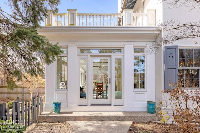 view of exterior entry featuring a balcony, fence, and stucco siding