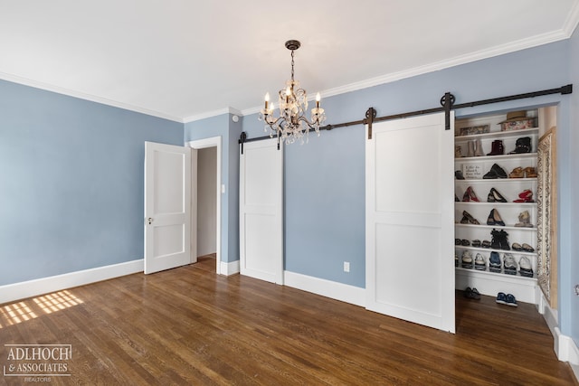 unfurnished room featuring baseboards, dark wood finished floors, ornamental molding, a barn door, and a notable chandelier