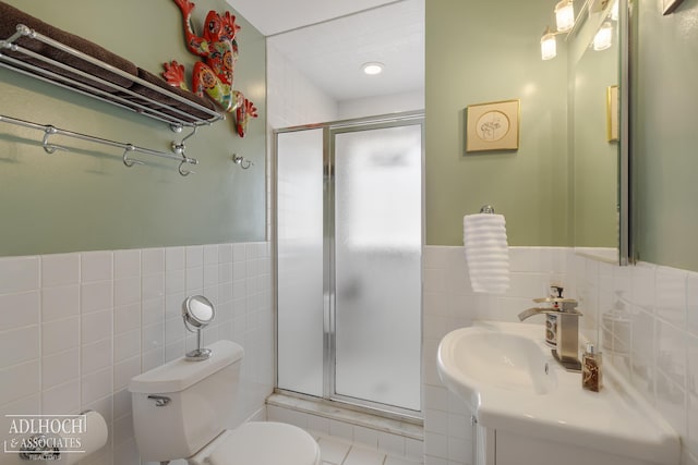 bathroom with a wainscoted wall, toilet, vanity, a stall shower, and tile walls