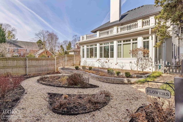 rear view of property featuring a balcony, a chimney, and fence