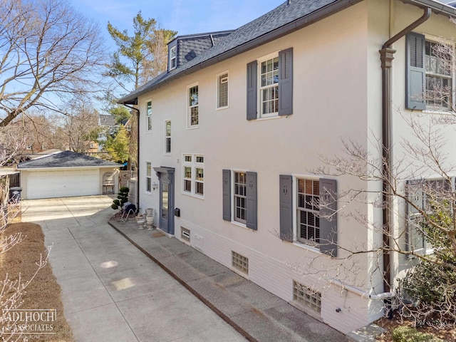 view of home's exterior with a garage, an outbuilding, a shingled roof, and stucco siding