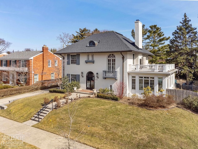 view of front facade featuring a chimney, a front yard, a balcony, and fence