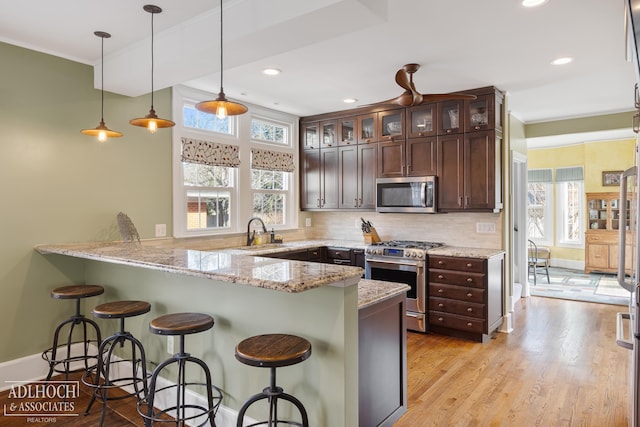 kitchen featuring decorative backsplash, a peninsula, dark brown cabinets, and appliances with stainless steel finishes